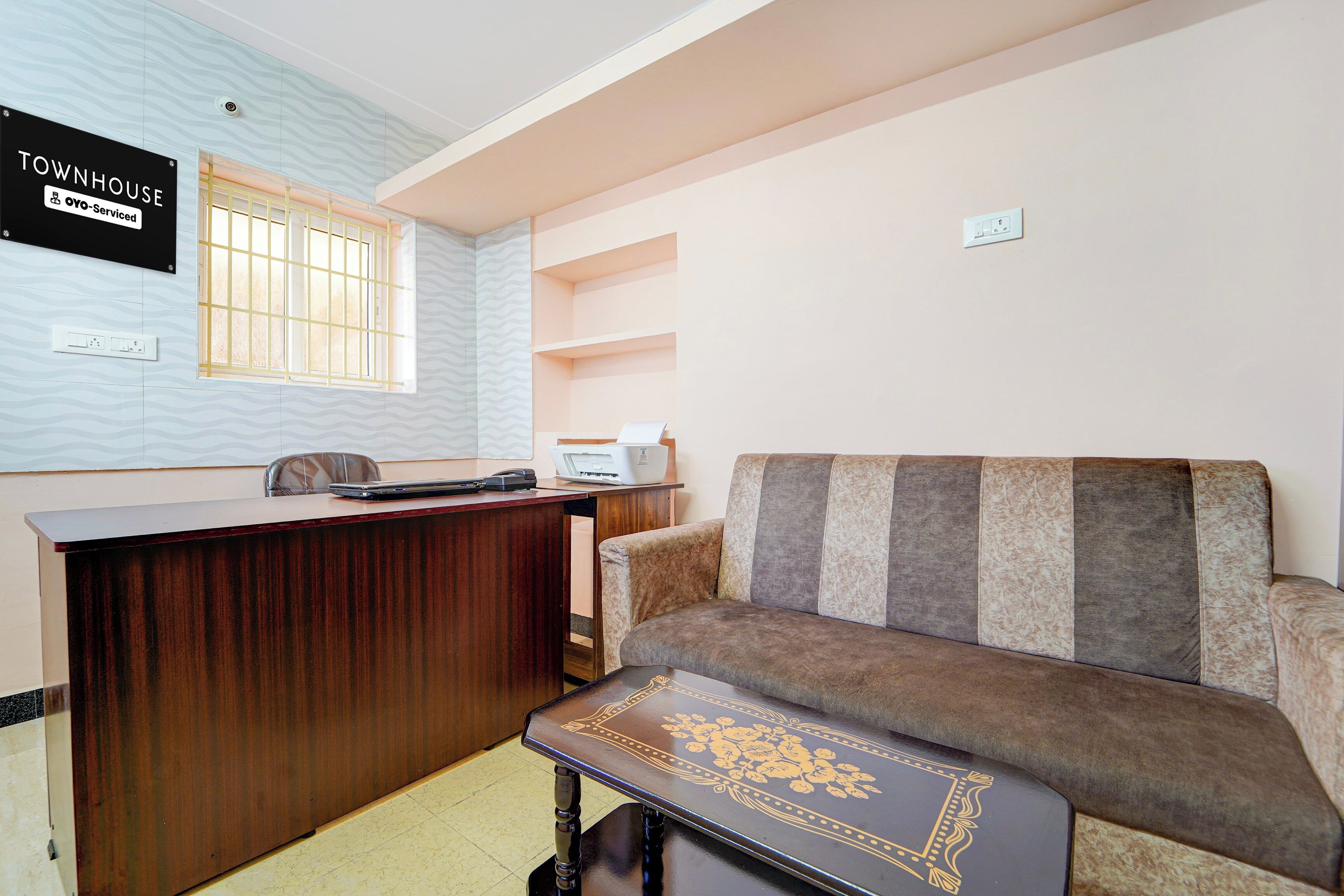 Een hotelkamer met een houten bureau, een bank, een aan de muur bevestigde televisie en een raam met tralies.