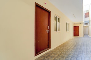 A corridor with wooden doors and windows, tiled flooring, and a ceiling with light fixtures.