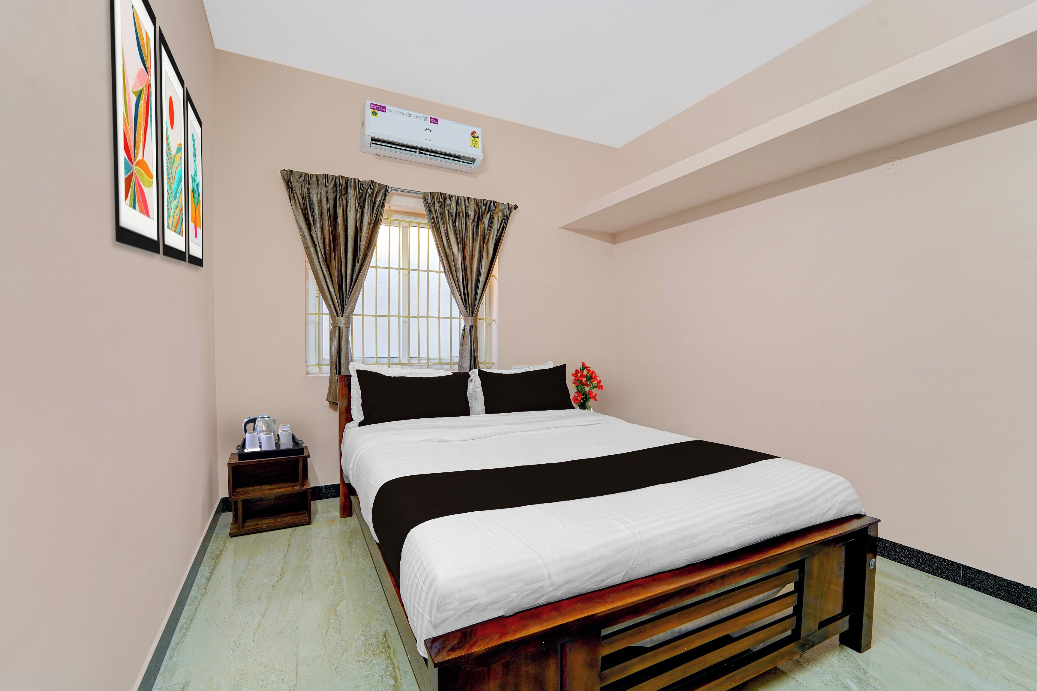 Habitación de hotel con cama, mesita de noche, ventana con cortinas, unidad de aire acondicionado y un cuadro en la pared.