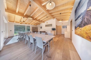 Una habitación amplia con una gran mesa de madera para comer, sillas modernas y un techo alto con vigas a la vista.