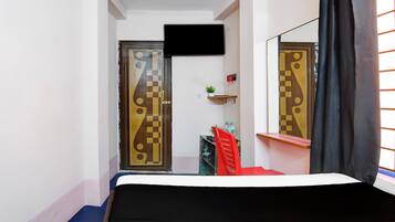 Una habitación con una cama, televisión instalada en la pared y una ventana con cortinas.