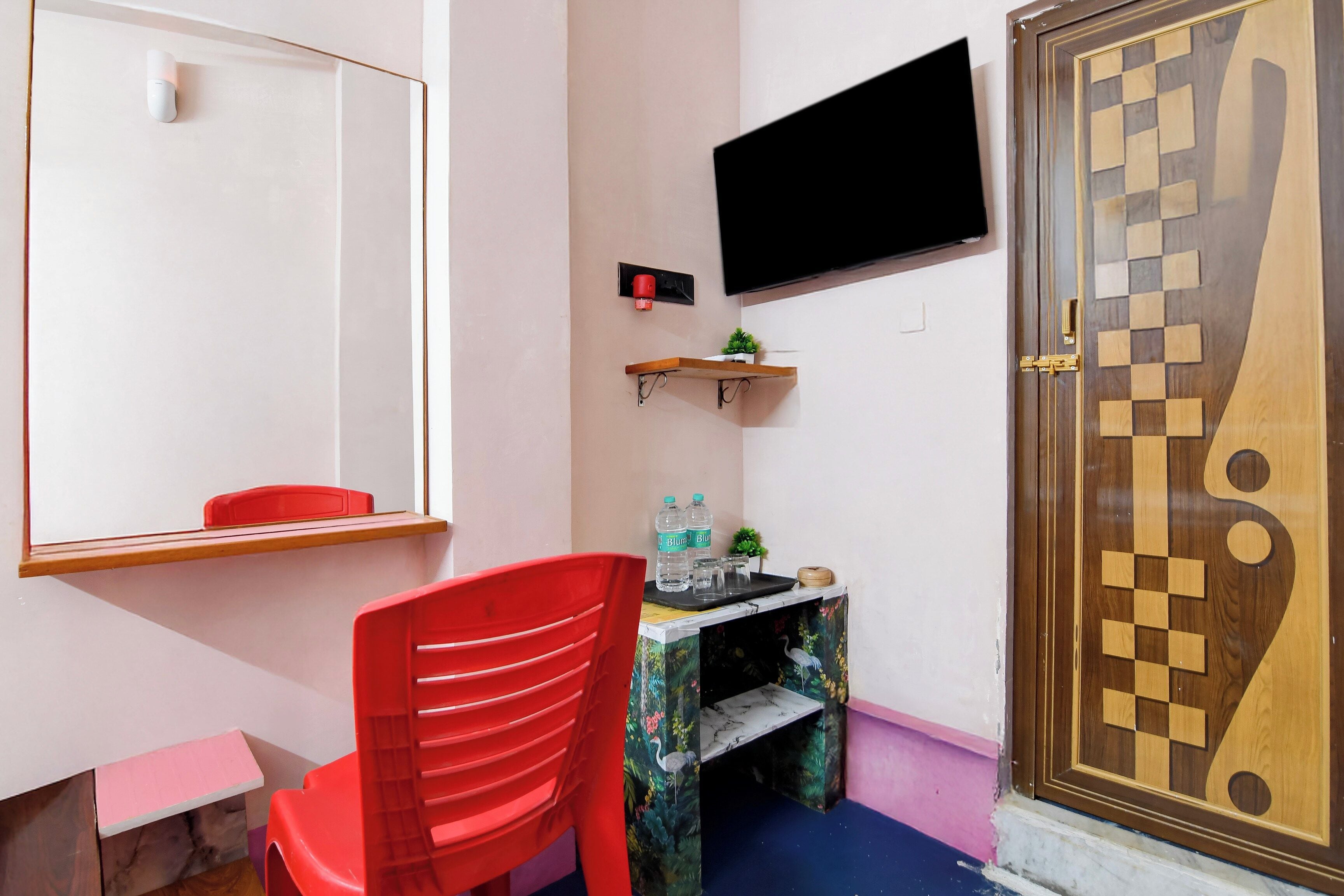 A small room with a red chair, a small table with water bottles, a mounted TV, and a decorative wooden door.