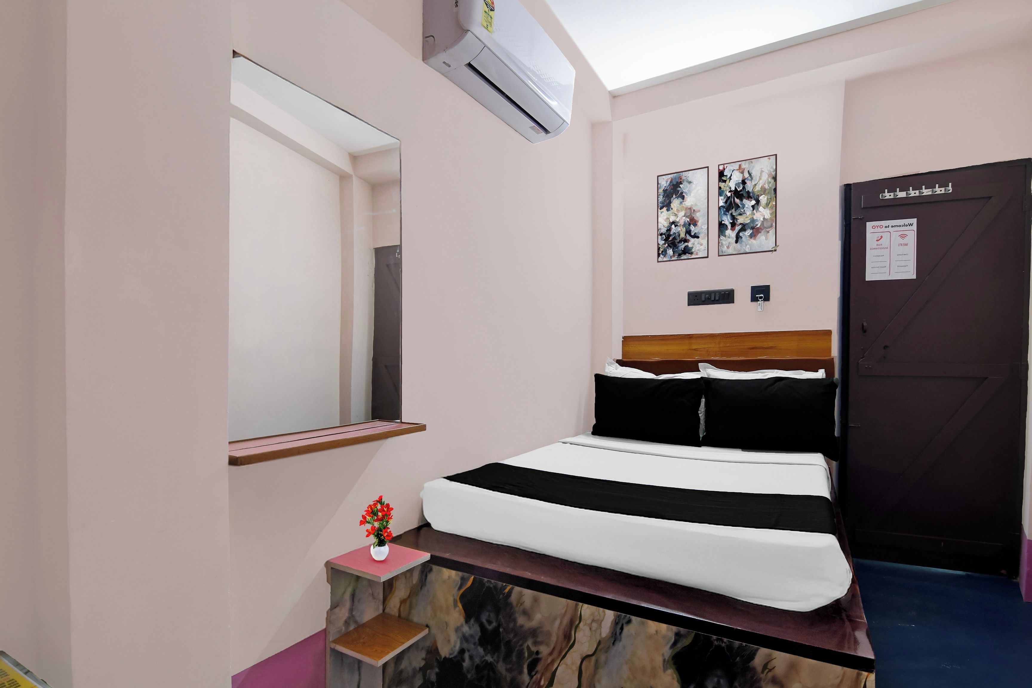 A bedroom with a bed, a nightstand, a mirror, a door, and two wall-mounted artworks.