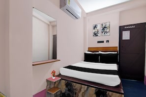 Un dormitorio con una cama, una mesita de noche, un espejo, una puerta y dos obras de arte colgadas en la pared.