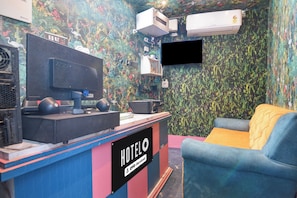 Una habitación de hotel con televisión, unidades de aire acondicionado, un escritorio con computadora y un sofá.