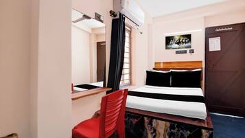 Habitación de hotel con cama, escritorio, silla, equipo de aire acondicionado, puerta y televisor montado en la pared.