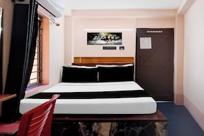 A hotel room with a bed, a desk, a chair, a window with curtains, a door, and a wall-mounted picture.