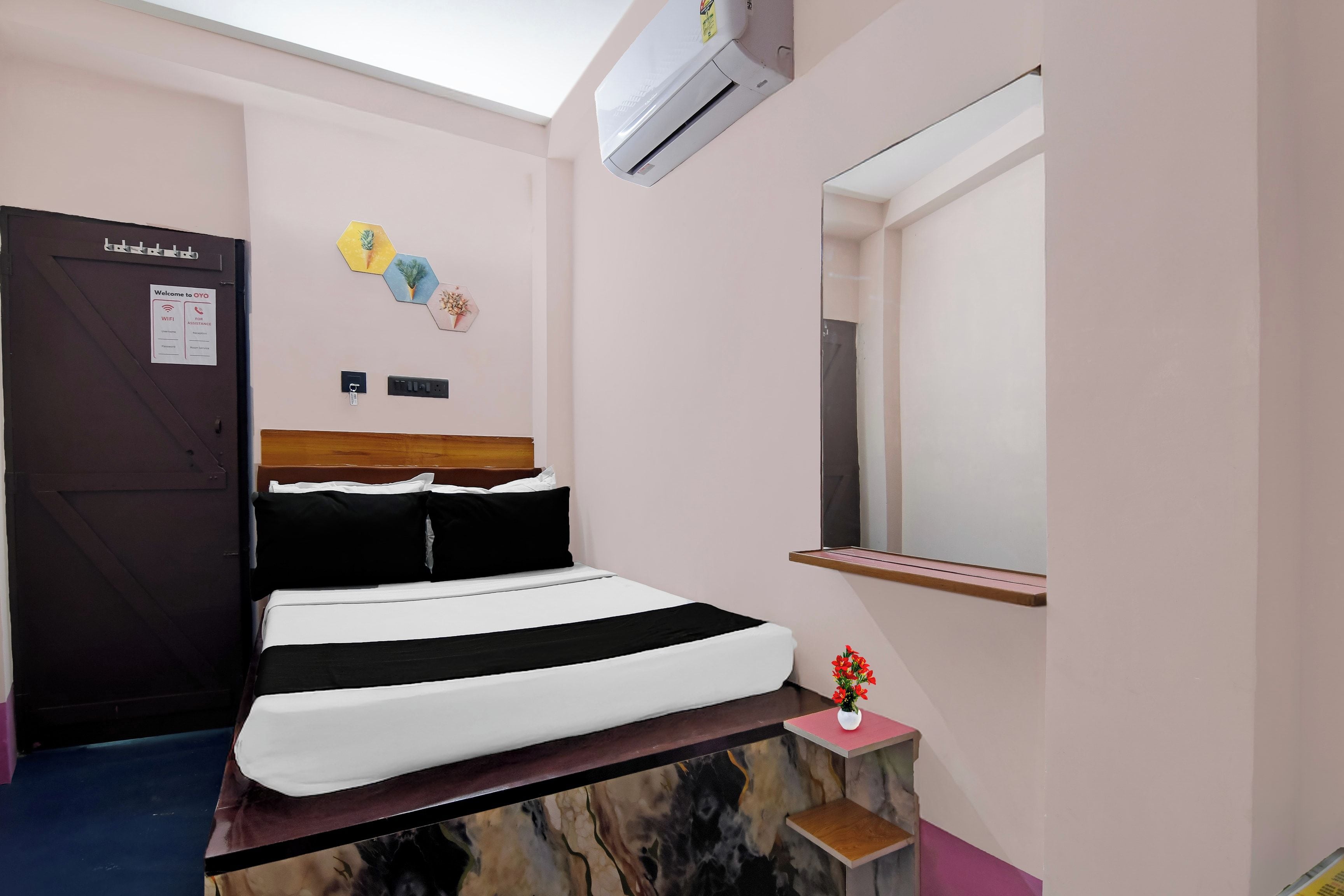 A hotel room with a bed, a bedside table, a mirror, a wall-mounted air conditioner, and a door with a sign.