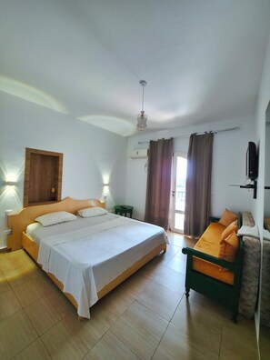 Quarto de hotel com uma cama grande, um sofá, uma televisão e um ventilador de teto.