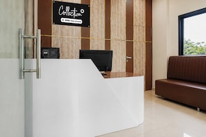 Una recepción con un cartel que indica que ofrece servicios OYO, una computadora, un ventanal con vistas y un banco tapizado en marrón.