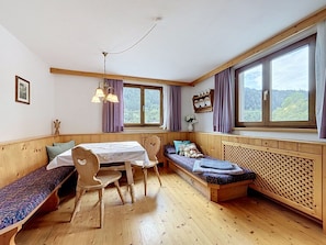Ein gemütliches Zimmer mit einer hölzernen Bank, einem Tisch mit Stühlen und einem Fenster mit Vorhängen.