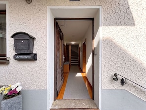 Ein Flur, der zu einer Treppe führt, an deren Wand ein Briefkasten mit der Aufschrift 'Zeitungen' angebracht ist.