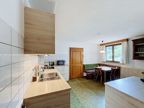 Eine kompakte Küche mit Holzschrank, Spüle, Mikrowelle und Essbereich mit Tisch und Stühlen.