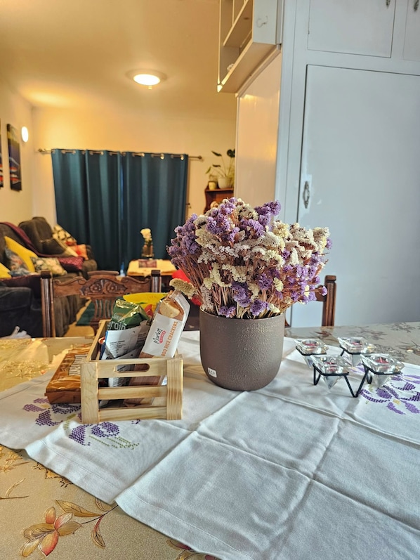 A living room with a floral arrangement on a table, a couch, and a dining area with a tablecloth.
