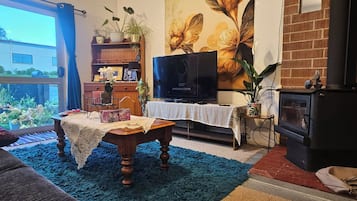 Una sala de estar con televisor, chimenea, mesa de comedor y un gran ventanal.