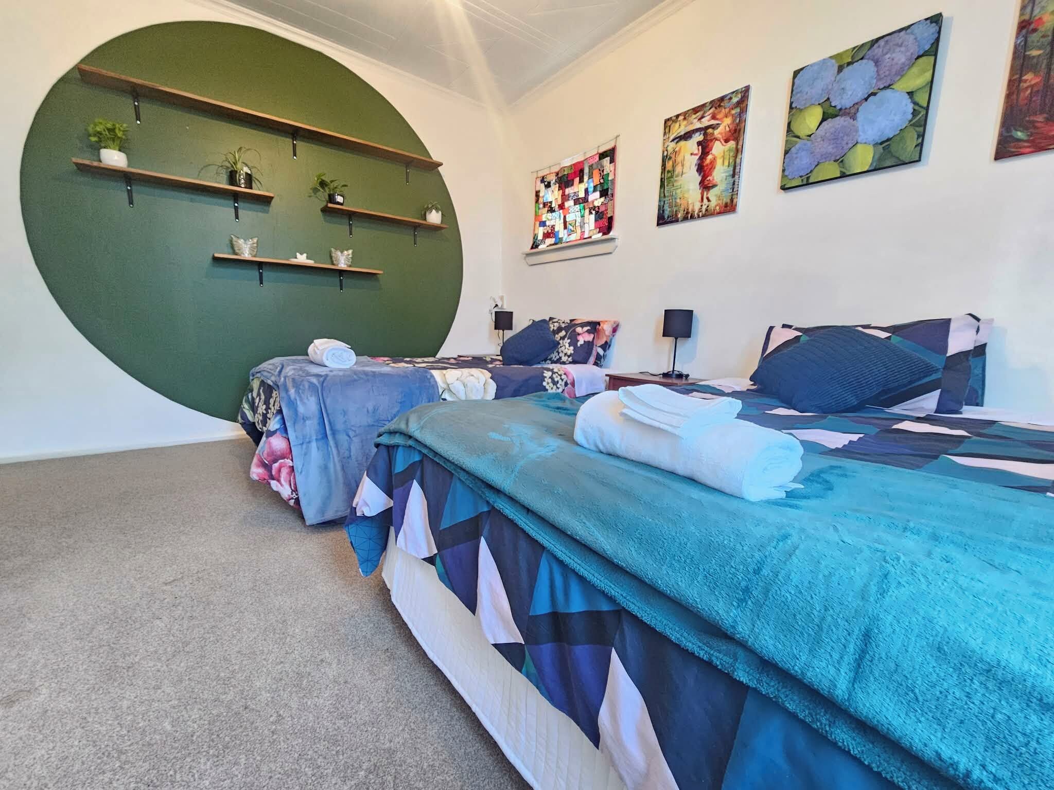 A modern bedroom with two beds, a green accent wall, and artwork.