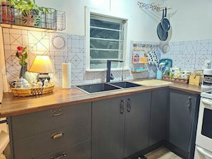 A kitchen with a wooden countertop, a sink, cabinets, a window, and a hanging pot rack.