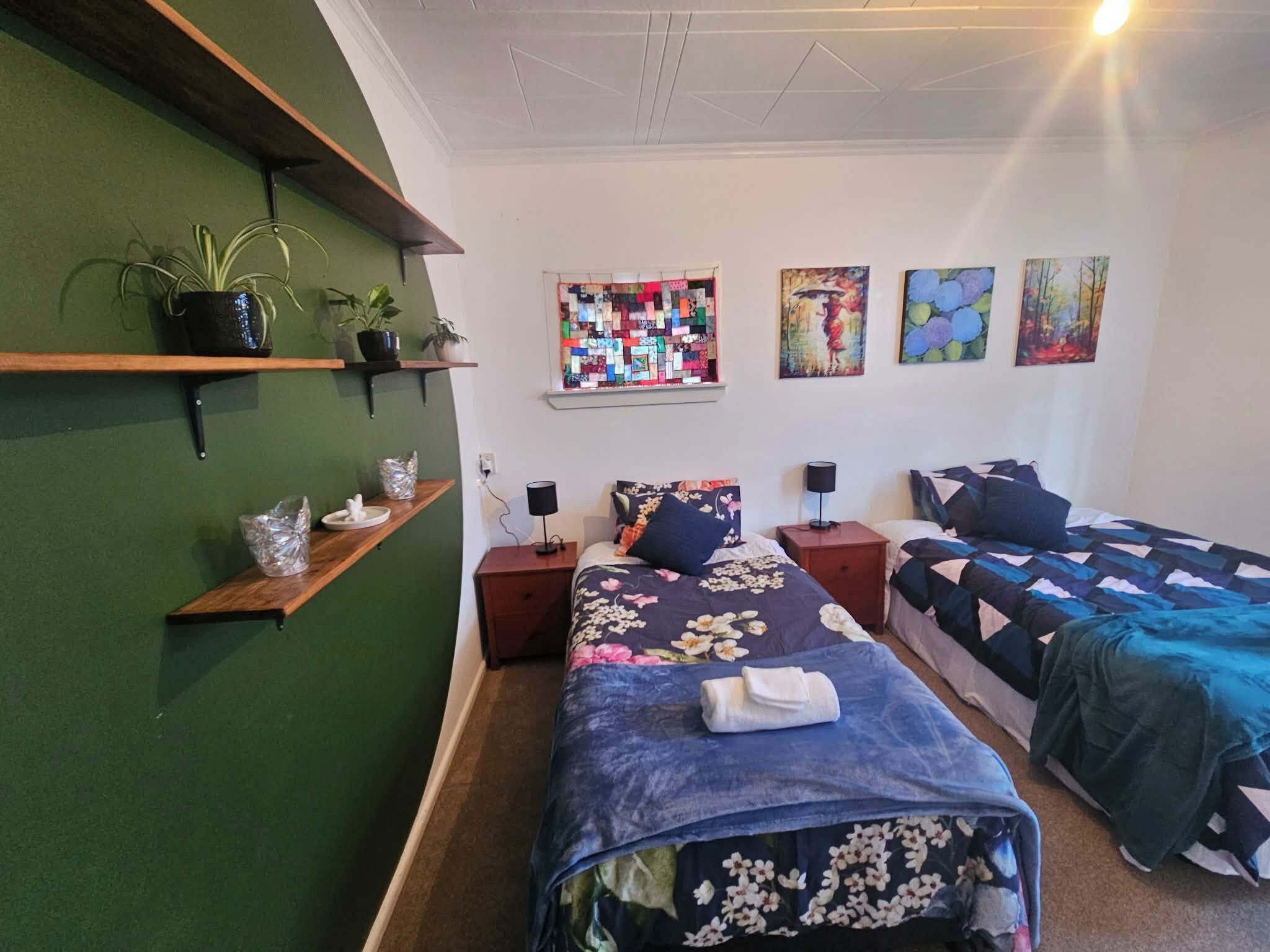 Ein Schlafzimmer mit zwei Betten, einer grünen Wand und einem gekettelten Fenster.