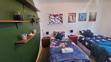 Ein Schlafzimmer mit zwei Betten, einer grünen Wand und einem gekettelten Fenster.