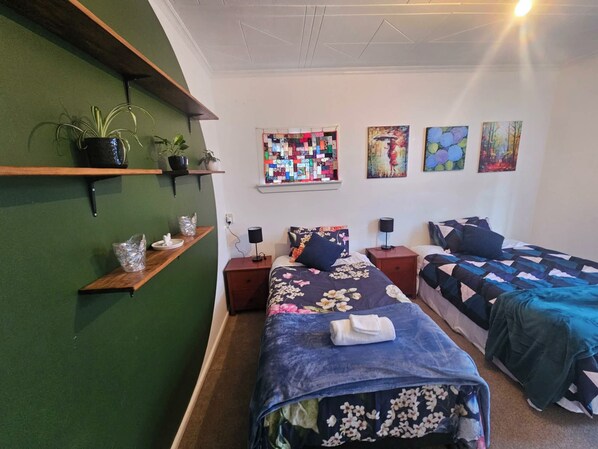 A bedroom with two beds, a green wall, and a quilted window.