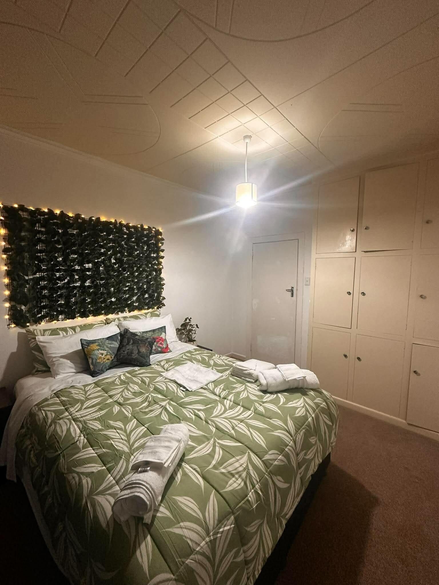 Ein Schlafzimmer mit einem Bett, einem Kopfteil mit Beleuchtung, einem Schrank und einer Decke mit Rasteroptik.
