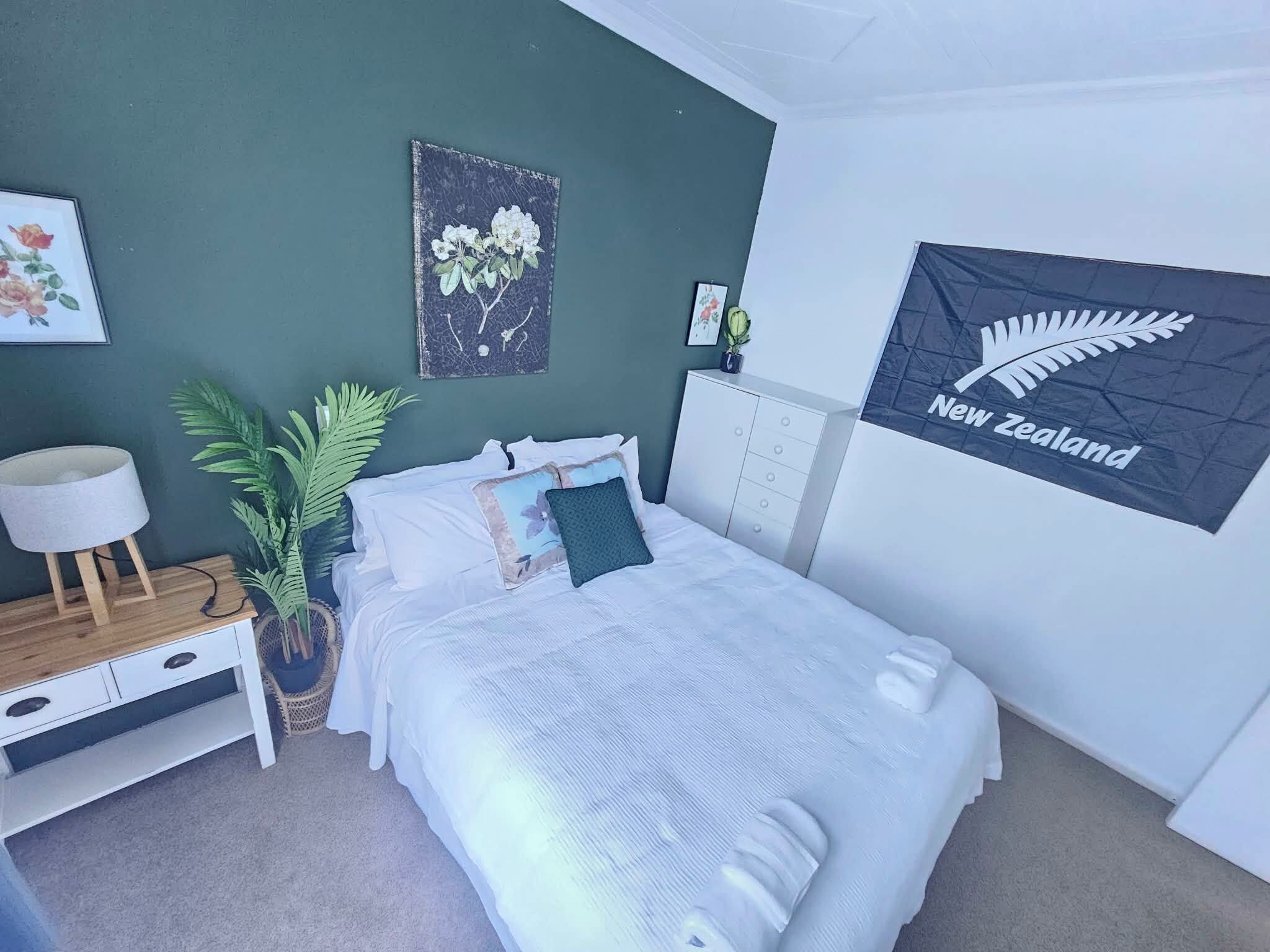 Un dormitorio con una cama, una mesita de noche, una lámpara, una planta en maceta y una pared con una bandera.