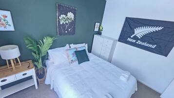 Un dormitorio con una cama, una mesita de noche, una lámpara, una planta en maceta y una pared con una bandera.