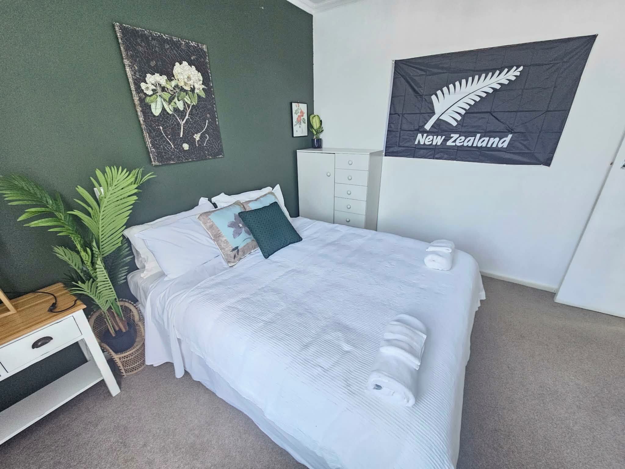 Quarto com cama, guarda-roupa, quadro emoldurado, planta em vaso e um objeto pendurado na parede.