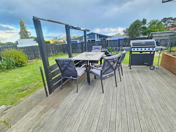A deck with a table and chairs, a barbecue grill, and a wooden fence.