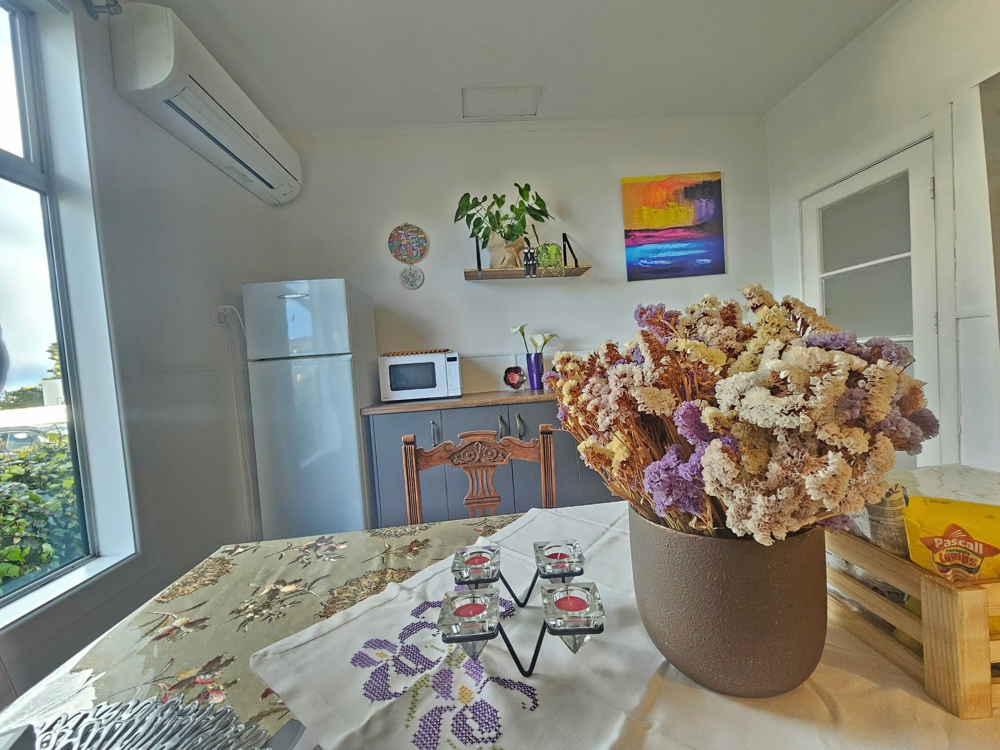 Keittiössä on jääkaappi, mikroaaltouuni ja ruokapöytä, jonka päällä on kukkakuviollinen pöytäliina.