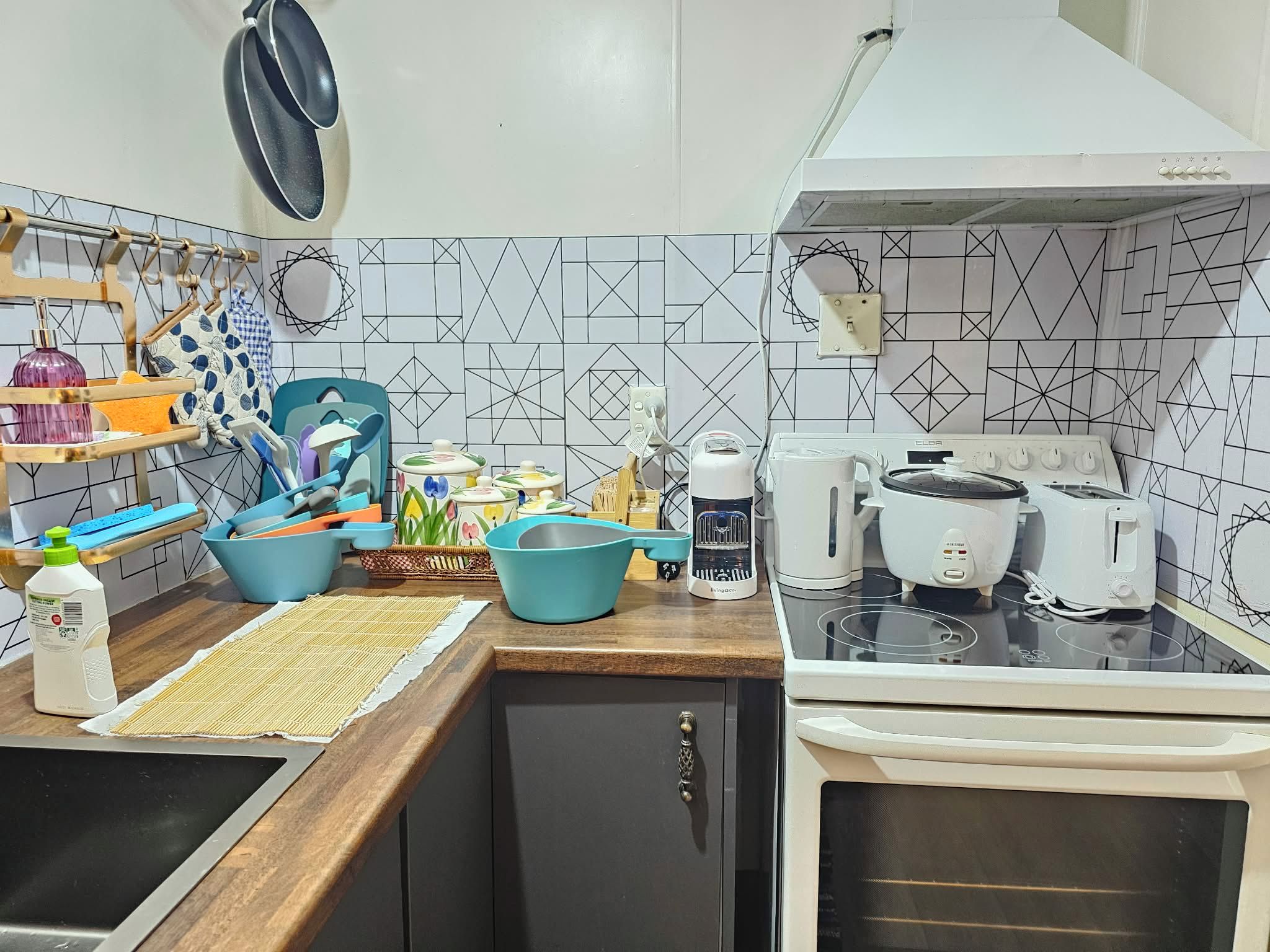 A kitchen with a stove, toaster, kettle, and various utensils and containers on the counter.