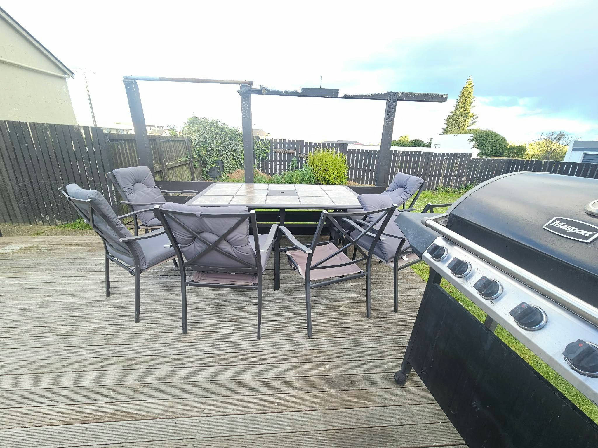 A patio with a table and chairs, a grill, and a wooden deck.