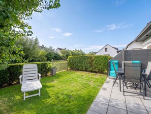 Ein Garten mit grünem Rasen, einem weißen Stuhl, einem Tisch mit Stühlen und einer Hecke.
