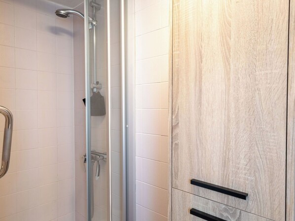 Eine Dusche mit Glastür, einem Handtuchhalter und einem Holzschrank mit zwei Schubladen.
