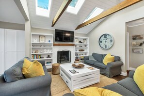 A modern living room with a fireplace, built-in shelves, a large wall clock, and a cozy seating area. - Lake Winnipesaukee Waterfront Sandy Beach 40 Ft Dock Sleeps 10 (Moultonborough)