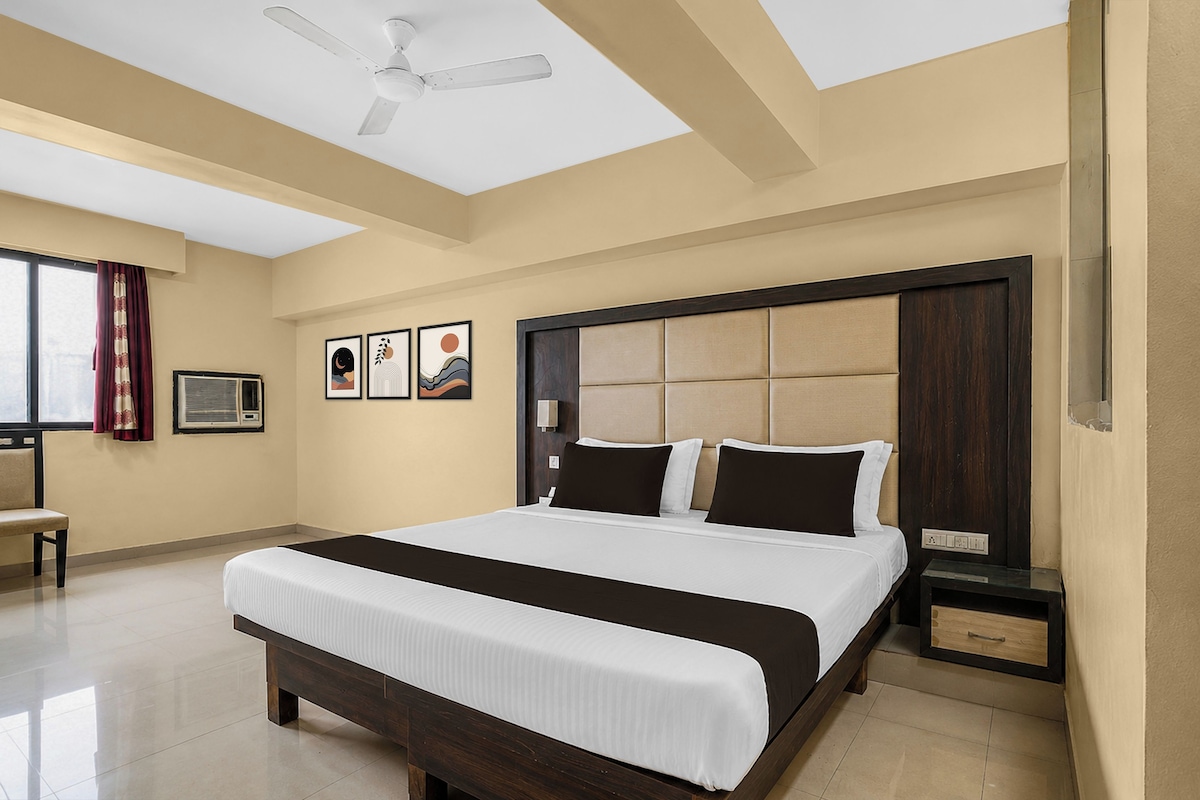 Habitación de hotel con una cama grande, ventilador de techo, ventana con cortinas y una obra de arte en la pared.