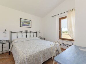 Ein Schlafzimmer mit einem Bett, einem Fenster mit Vorhängen, einem Bild an der Wand und einem Tisch mit einem Stuhl.