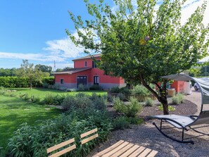 Een rood gebouw met een tuin, een bankje en een boom.