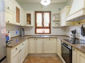 Een keuken met witte kastjes, een raam met gordijnen, een spoelbak en een fornuis.