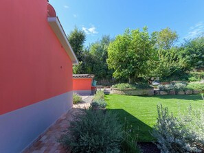 Ein Garten mit einem roten Gebäude, einer Rasenfläche und verschiedenen Pflanzen.