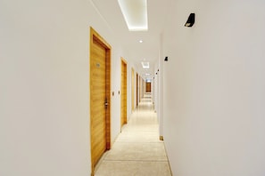 Um corredor comprido e estreito, com portas de madeira e paredes brancas.