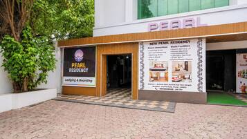 A Pearl Residency building with a checkered pavement in front, a signboard with amenities, and a large window above the entrance.