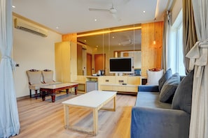 Uma sala de estar moderna com sofá, mesa de centro, televisão e cozinha com armários de madeira.