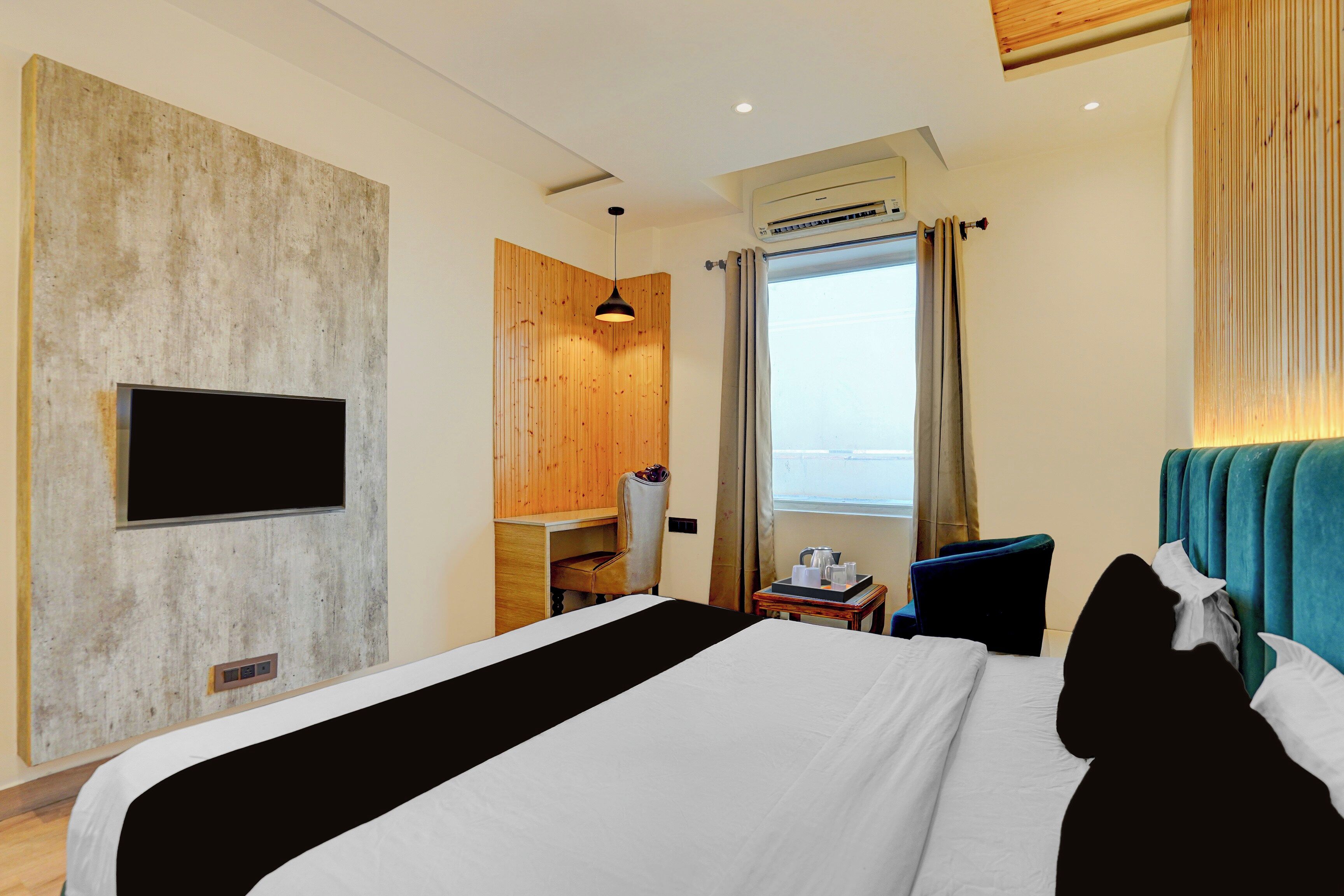 Habitación de hotel con cama, escritorio, silla, televisor, ventana con cortinas y equipo de aire acondicionado.