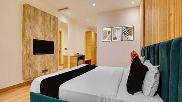 Habitación de hotel con cama, televisor montado en la pared, escritorio y una pequeña cocina.