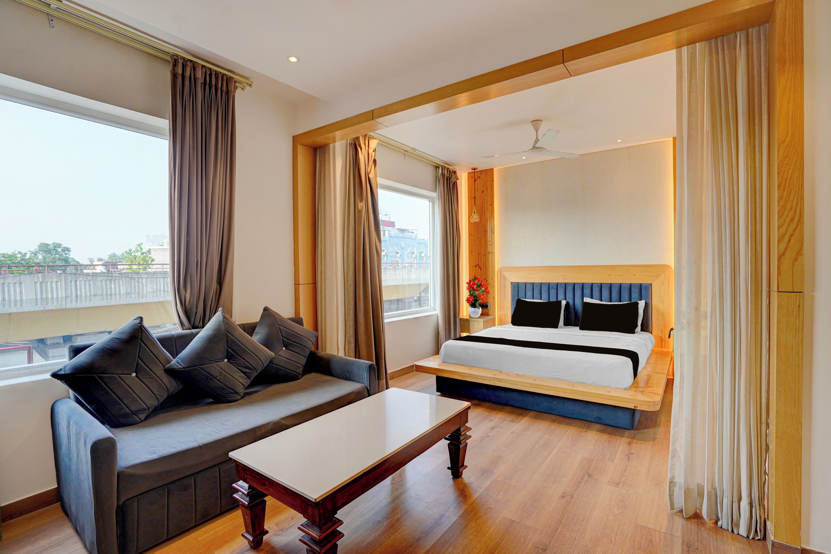 A hotel room with a bed, a sofa, a table, and a view of the city.