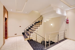 Escadaria moderna com corrimão de metal e extintor fixado na parede, além de piso revestido com azulejos.