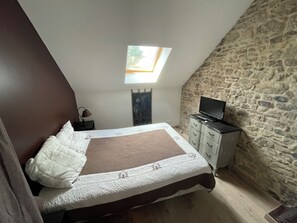 A bedroom with a sloped ceiling, a skylight, a bed with a quilt, a dresser, and a television.