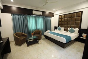 Una habitación de hotel con una cama, dos sillones, una mesita y un ventilador de techo.