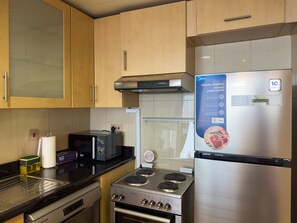 A kitchen with a stainless steel refrigerator, a gas stove, a microwave, and wooden cabinets. - Vanilla Homes Luxury 2BR in Reem Island (Abu Dhabi)